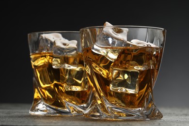 Whiskey and ice cubes in glasses on grey textured table, closeup