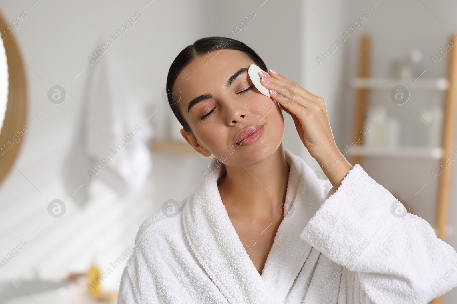 Photo of Beautiful woman removing makeup with cotton pad in bathroom, space for text