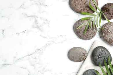 Photo of Spa stones with water drops and green leaves on white marble table, flat lay. Space for text