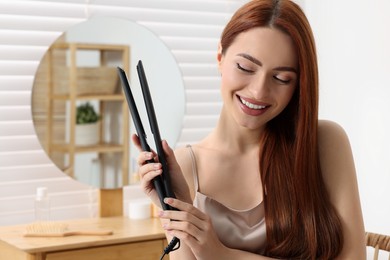 Photo of Beautiful woman with hair iron in room, space for text