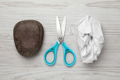 Photo of Rock, crumpled paper and scissors on wooden background, flat lay