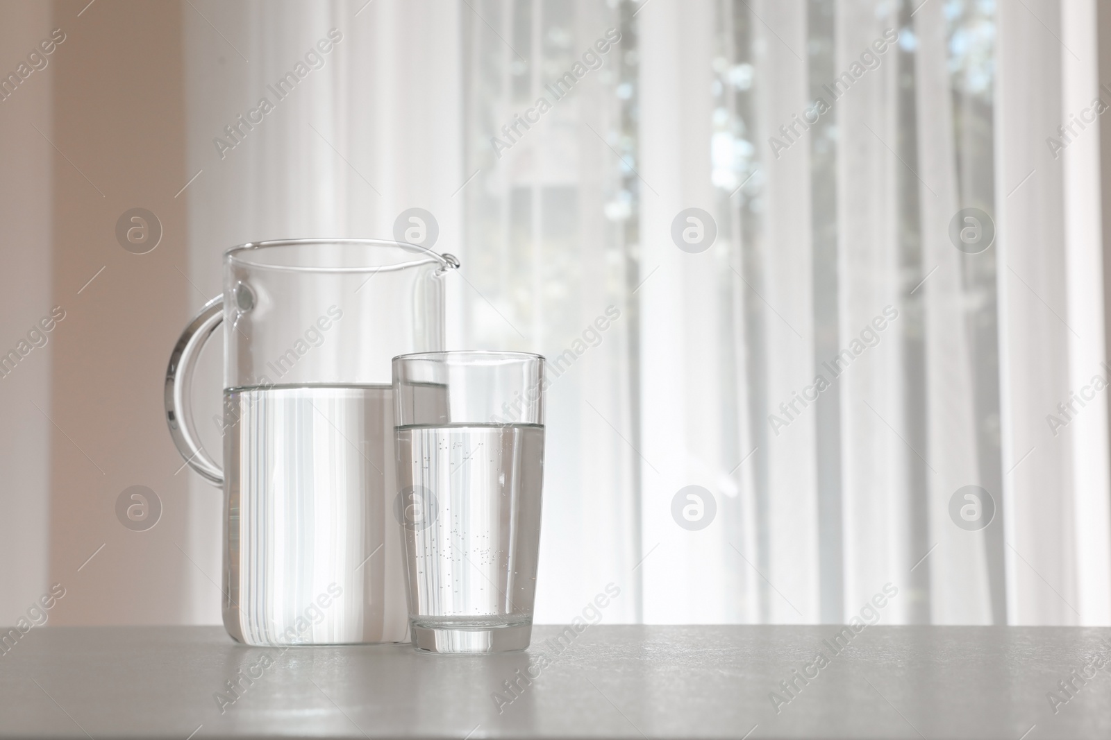 Photo of Jug and glass with water on table indoors. Space for text