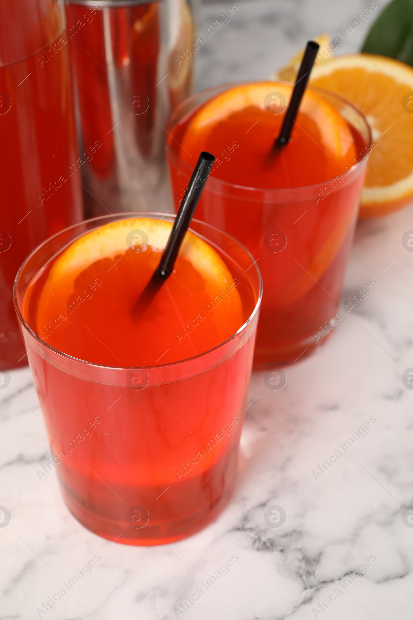 Photo of Aperol spritz cocktail, orange slices and straws in glasses on white marble table, closeup