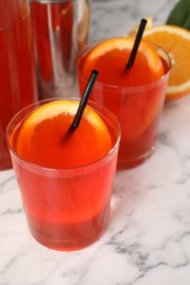 Aperol spritz cocktail, orange slices and straws in glasses on white marble table, closeup