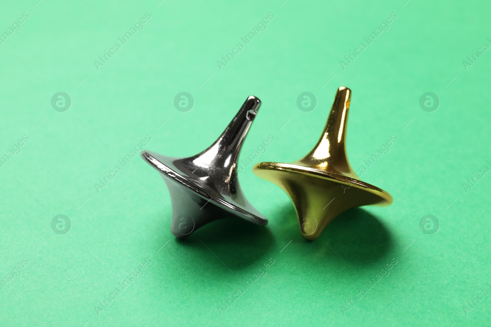 Photo of Golden and silver spinning tops on green background, closeup