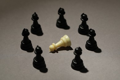 Photo of Black chess pieces and white one on grey background. Bullying concept