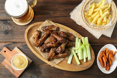 Delicious chicken wings served with beer on wooden table, flat lay