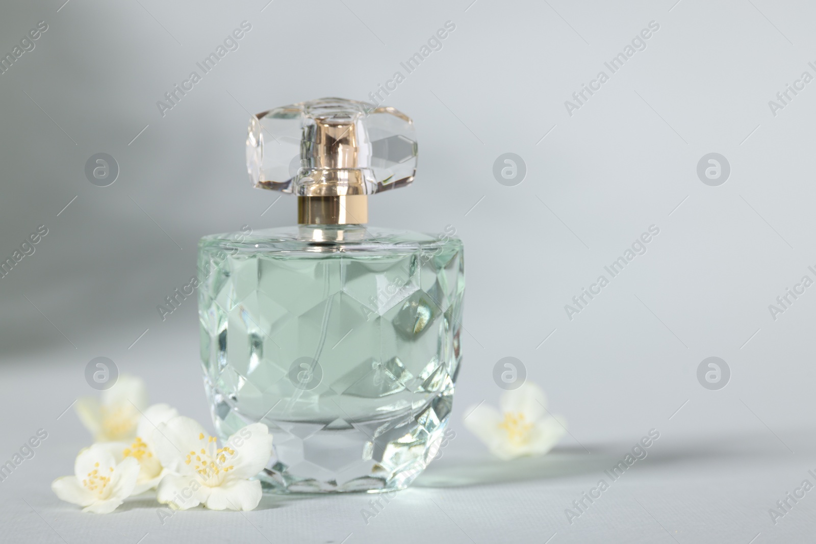 Photo of Aromatic perfume in bottle and beautiful jasmine flowers on grey background, closeup. Space for text