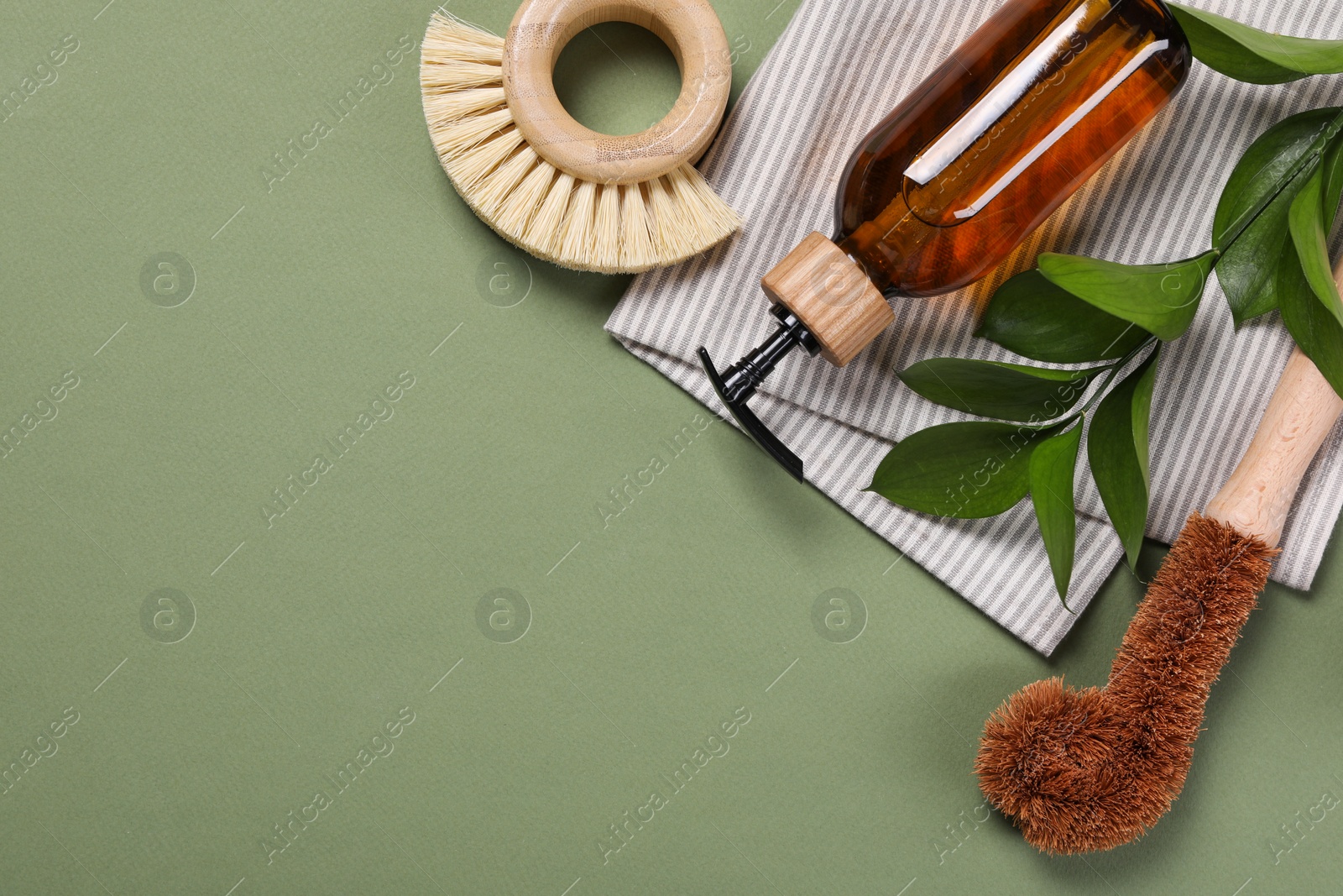 Photo of Cleaning brushes, dispenser, towel and leaves on green background, top view. Space for text