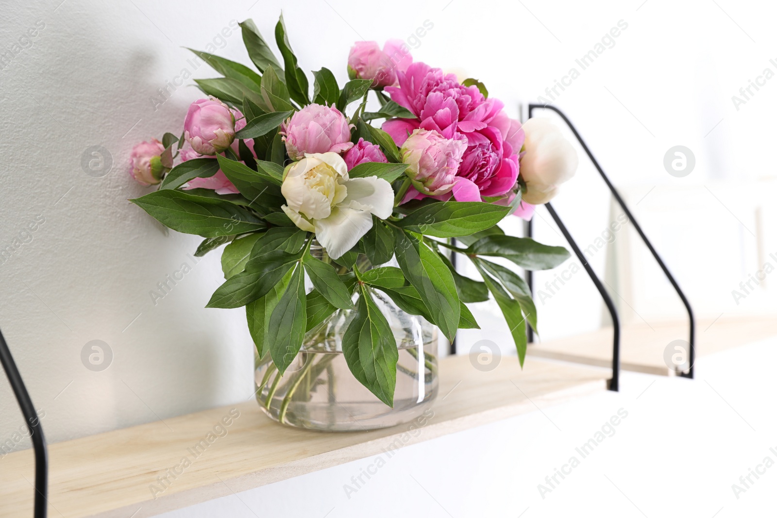 Photo of Shelf with vase of beautiful peonies on white wall