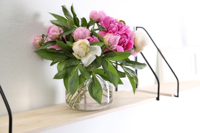 Photo of Shelf with vase of beautiful peonies on white wall