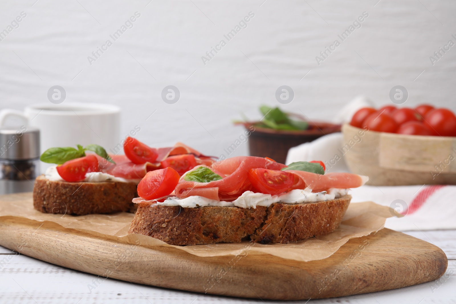 Photo of Tasty bruschettas with prosciutto, tomatoes and cheese on white wooden table
