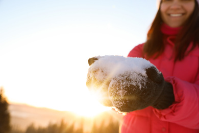 Photo of Woman holding pile of snow outdoors, closeup view with space for text. Winter vacation