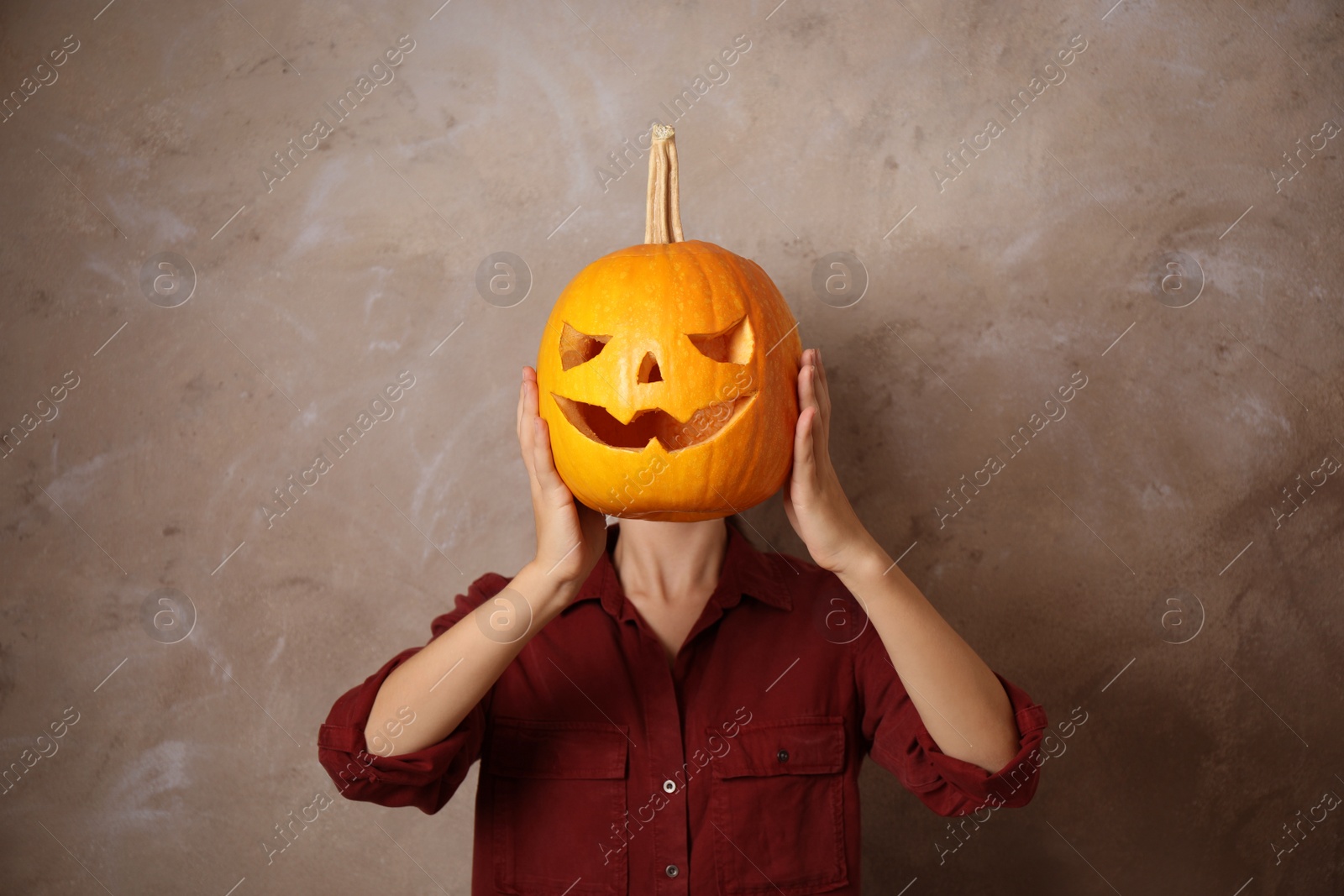 Photo of Woman with pumpkin head against beige background. Jack lantern - traditional Halloween decor