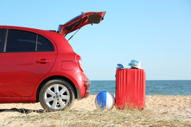 Modern car, bright suitcase and beach accessories on sand near sea