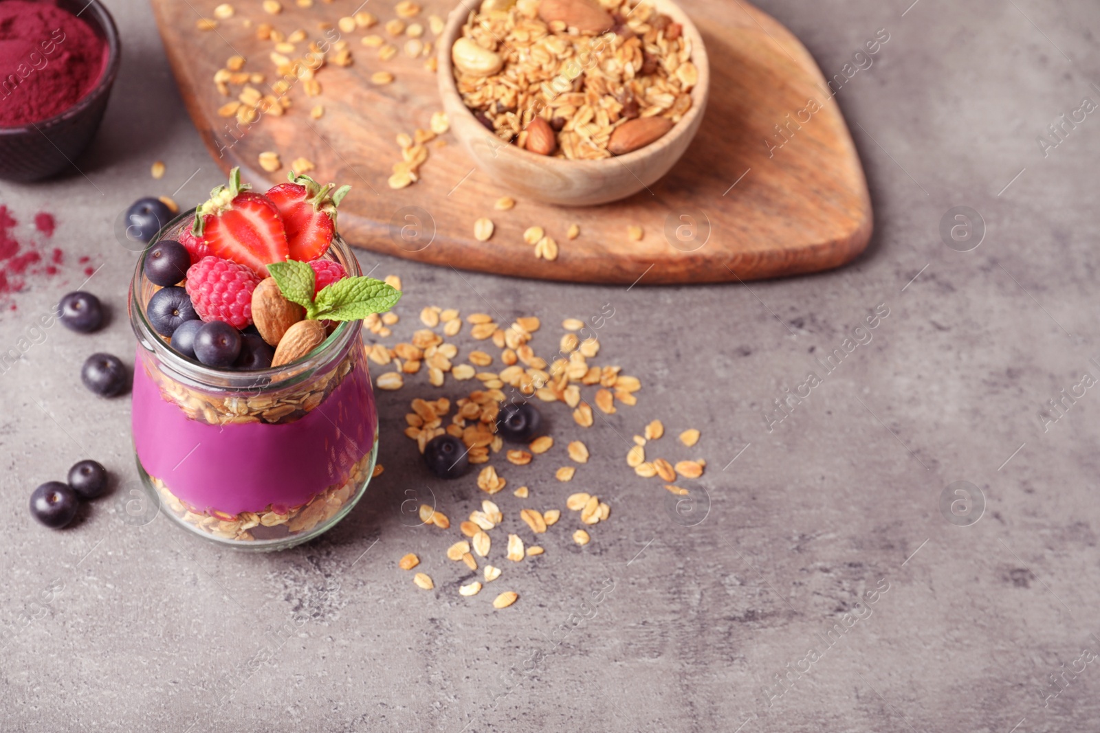 Photo of Delicious acai dessert with granola and berries served on grey table. Space for text