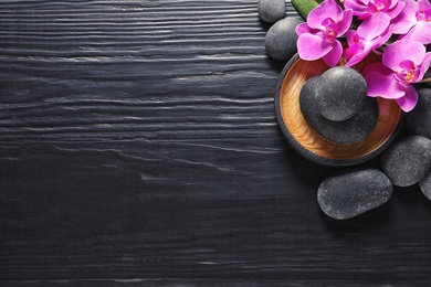 Composition with orchid flowers and spa stones on dark wooden background, top view. Space for text