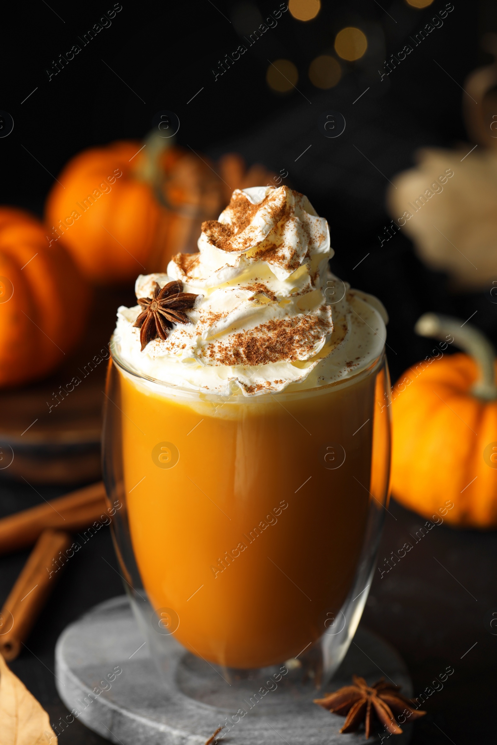 Photo of Glass of pumpkin spice latte with whipped cream and ingredients on black table, closeup