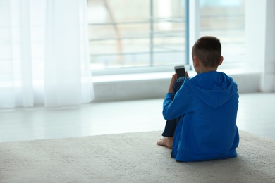 Photo of Upset boy with smartphone sitting near window indoors. Space for text