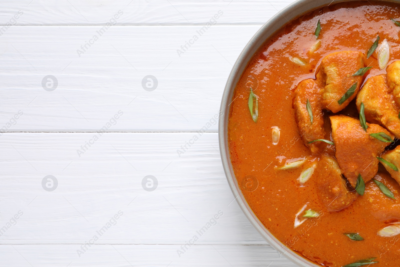 Photo of Bowl of delicious chicken curry on white wooden table, top view. Space for text