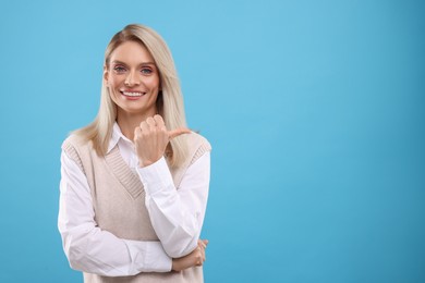 Photo of Portrait of smiling middle aged woman pointing at something on light blue background. Space for text