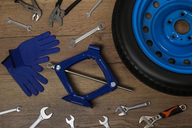 Photo of Car wheel, scissor jack, gloves and different tools on wooden surface, flat lay