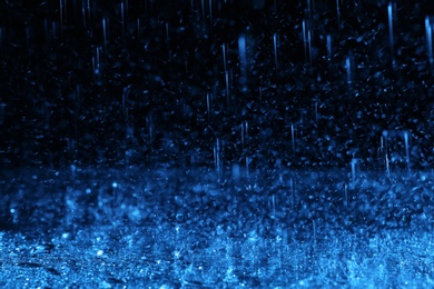 Photo of Heavy rain falling down on ground against dark background, toned in blue