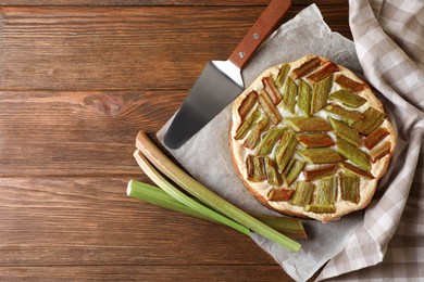 Photo of Freshly baked rhubarb pie, stalks and spatula on wooden table, flat lay. Space for text