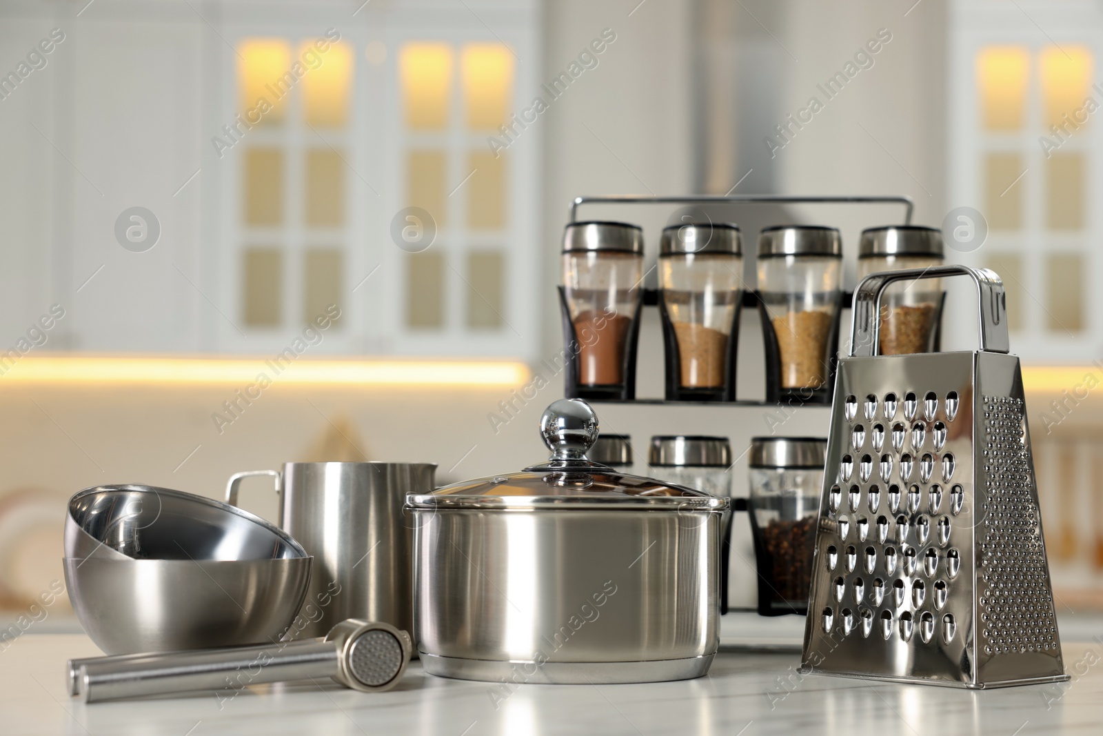 Photo of Set of shiny cooking utensils and spices on white table against blurred background