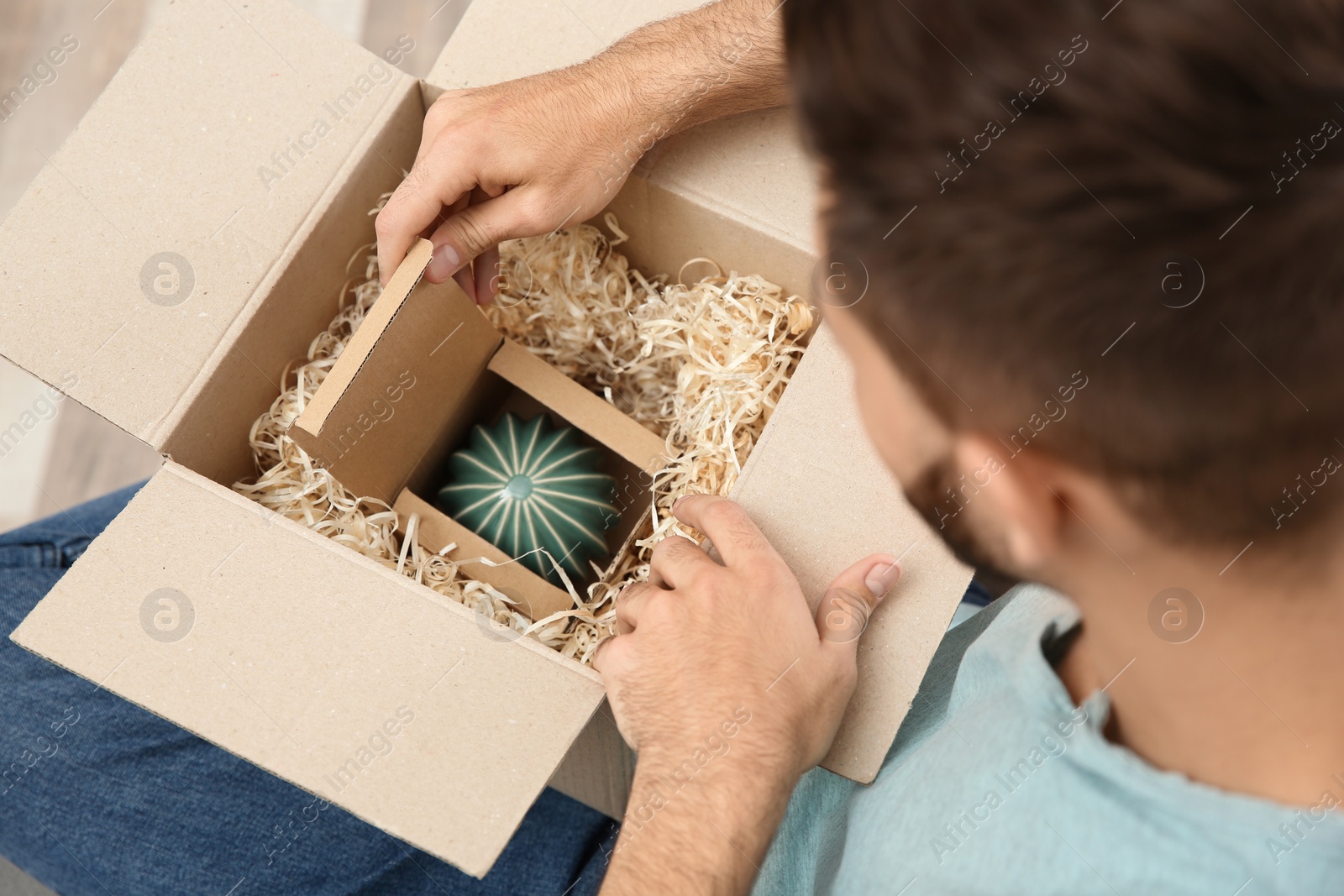 Photo of Young man opening parcel at home, closeup