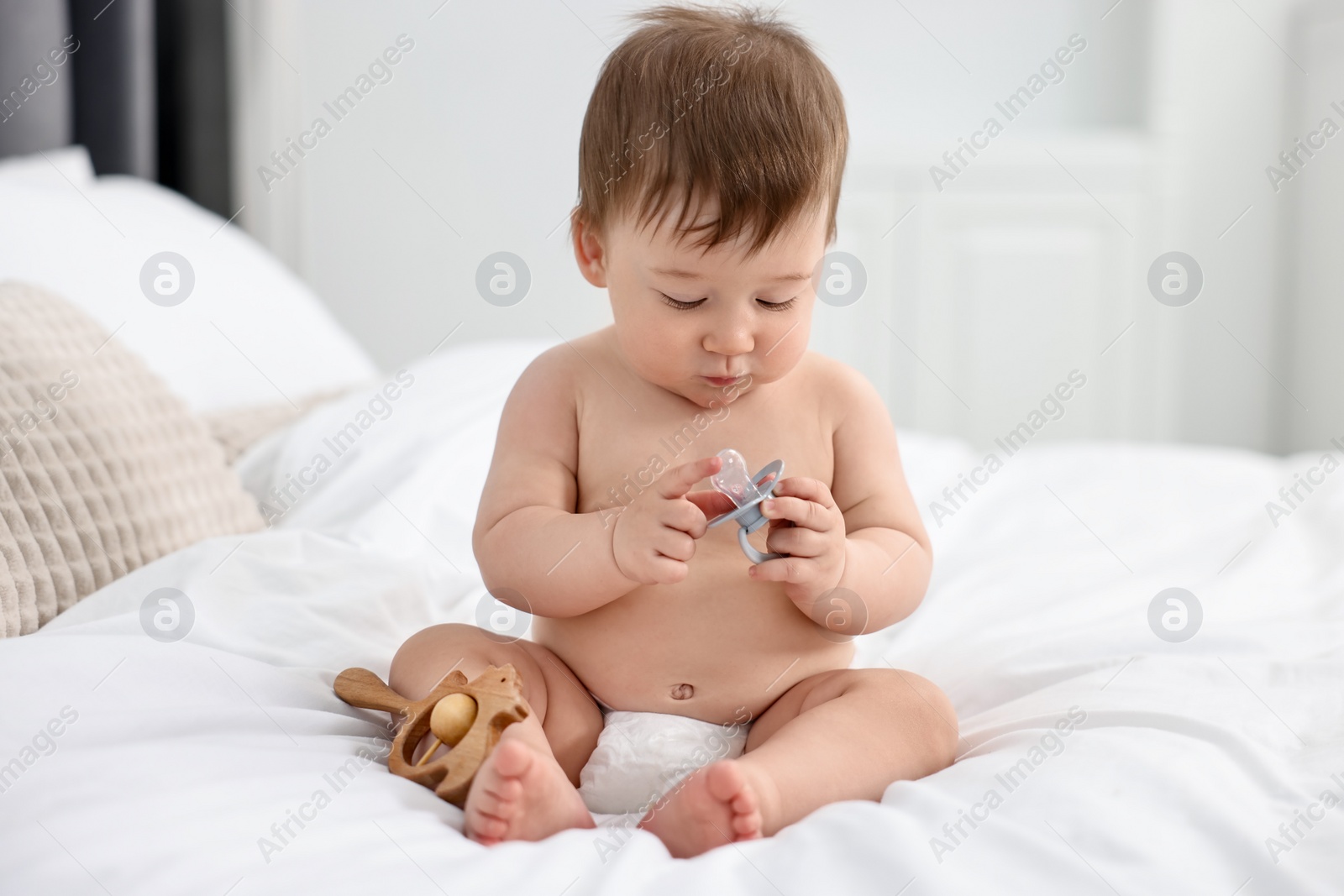 Photo of Cute baby boy with pacifier and wooden rattle on bed at home