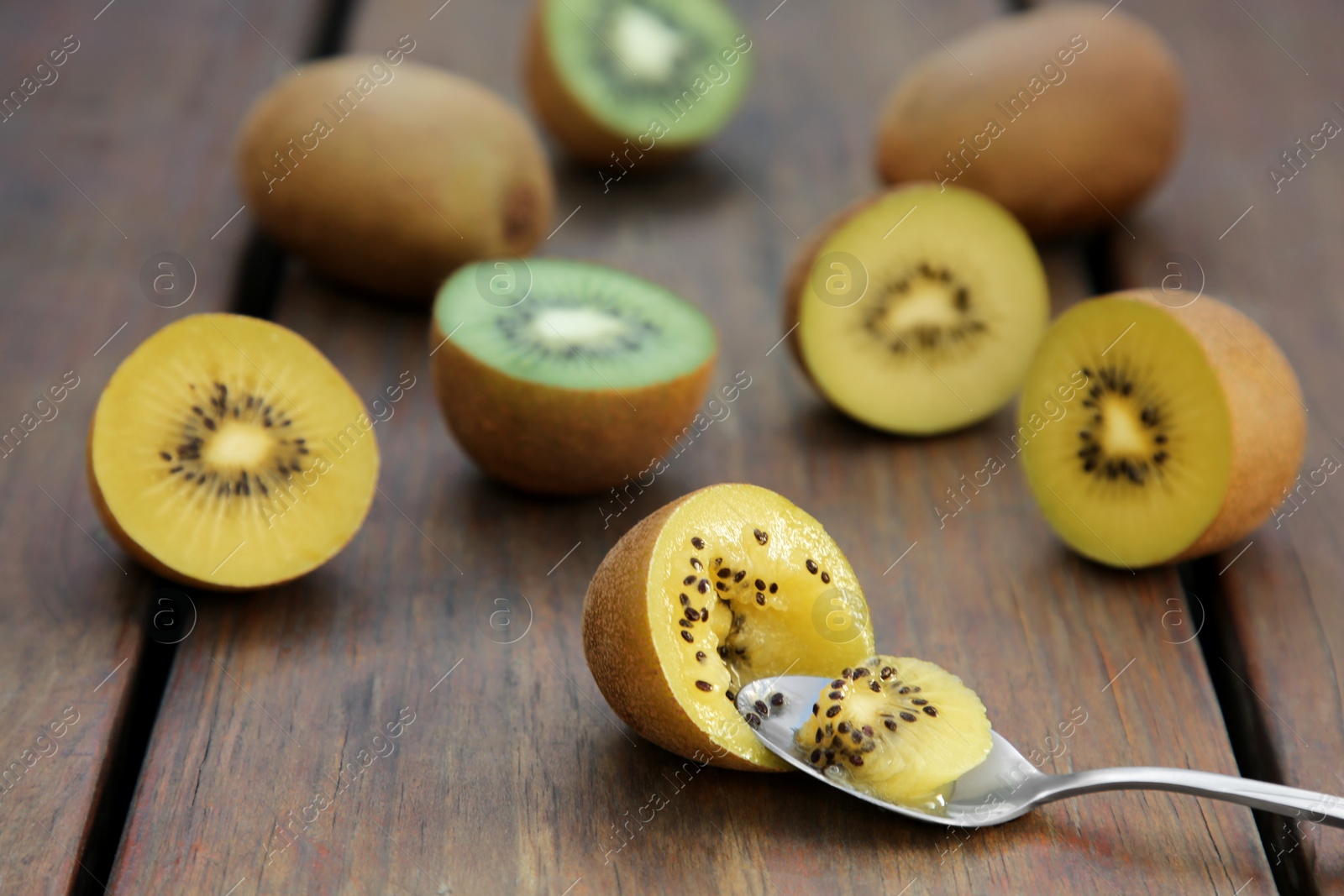 Photo of Spoon with half of kiwi and fruits on wooden table