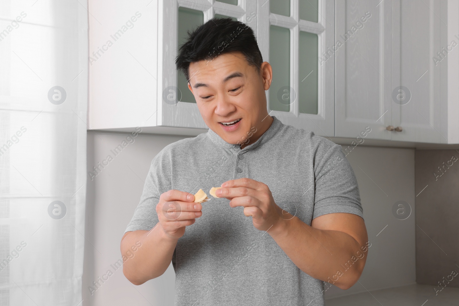 Photo of Emotional asian man holding tasty fortune cookie with prediction indoors