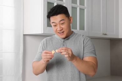 Emotional asian man holding tasty fortune cookie with prediction indoors