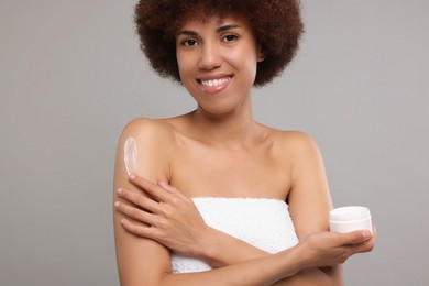 Photo of Beautiful young woman applying body cream onto arm on grey background