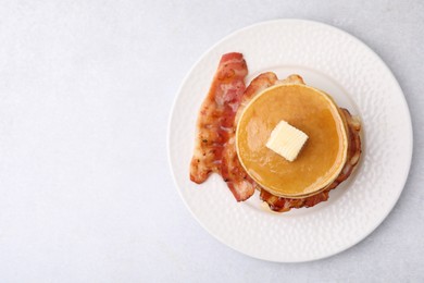 Delicious pancakes with bacon, butter and honey on light table, top view. Space for text