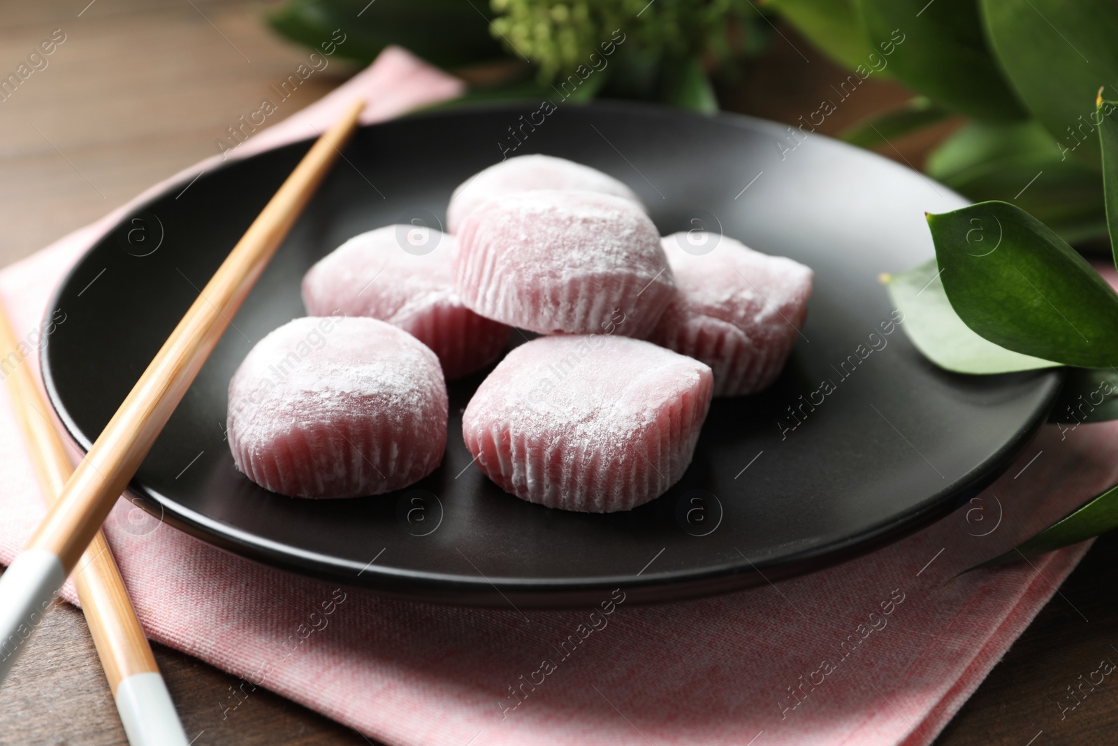 Photo of Black plate with delicious mochi and chopsticks on wooden table. Traditional Japanese dessert