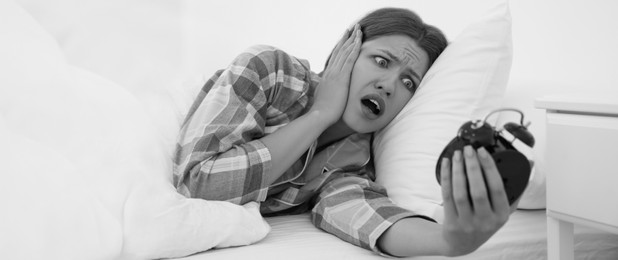 Emotional young woman with alarm clock at home in morning. Black and white photography