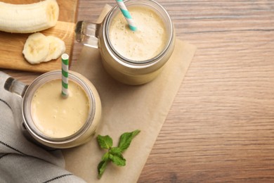 Photo of Tasty banana smoothie and mint on wooden table, flay lay. Space for text