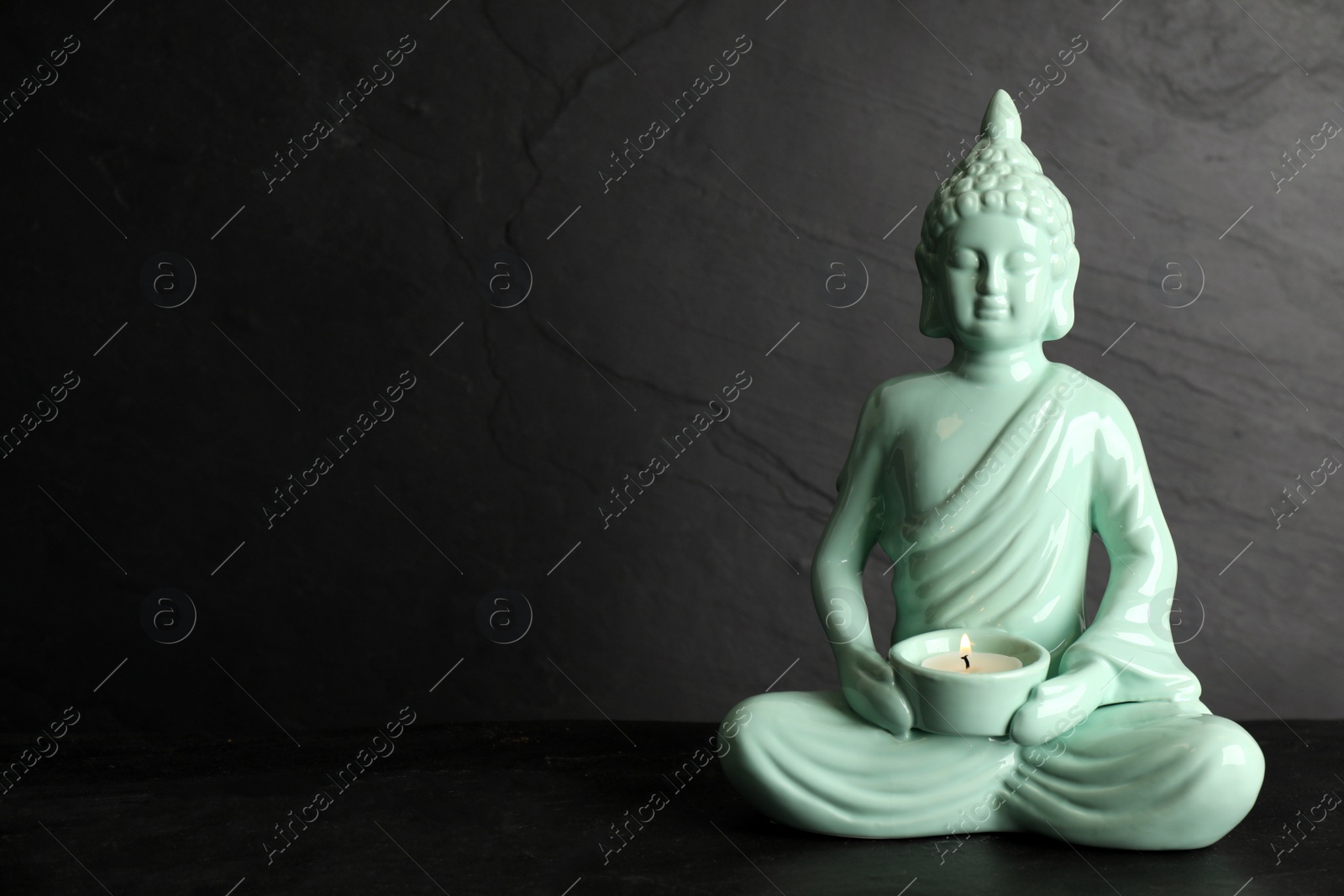 Photo of Buddha statue with burning candle on black table. Space for text