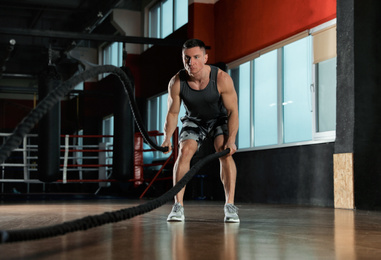 Photo of Man working out with battle ropes in modern gym