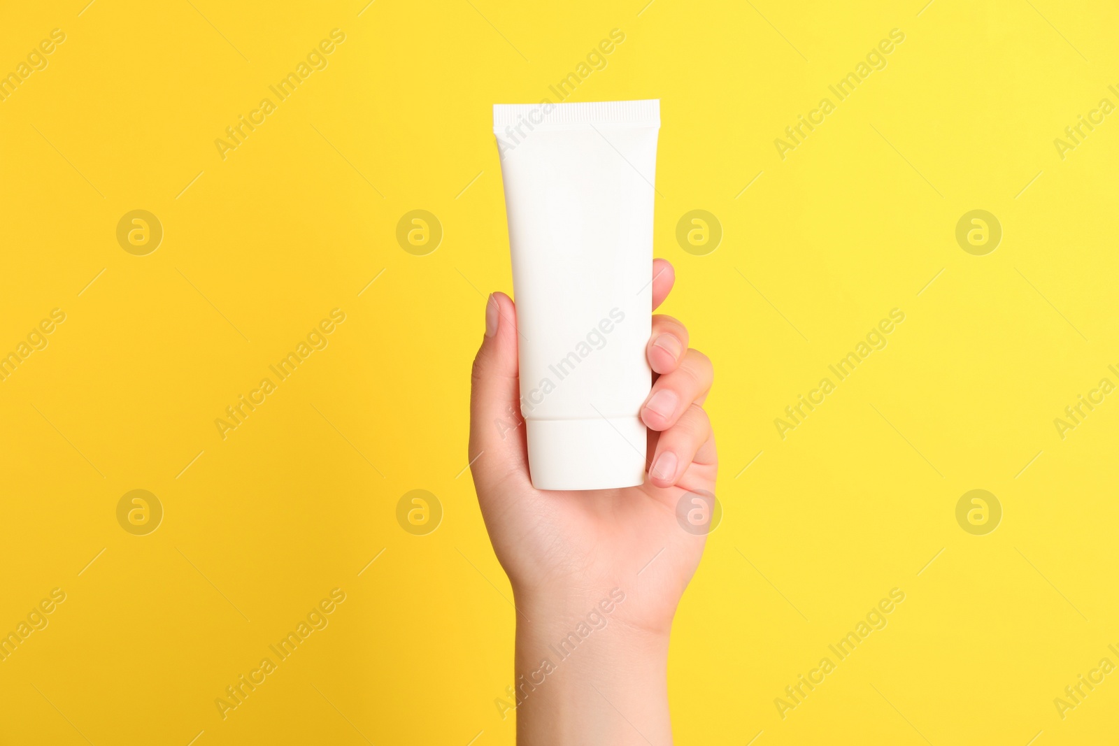 Photo of Woman holding tube of face cream on yellow background, closeup