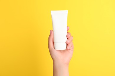 Photo of Woman holding tube of face cream on yellow background, closeup