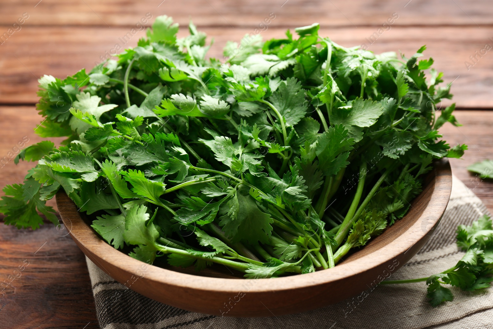 Photo of Fresh coriander in bowl on wooden table, closeup