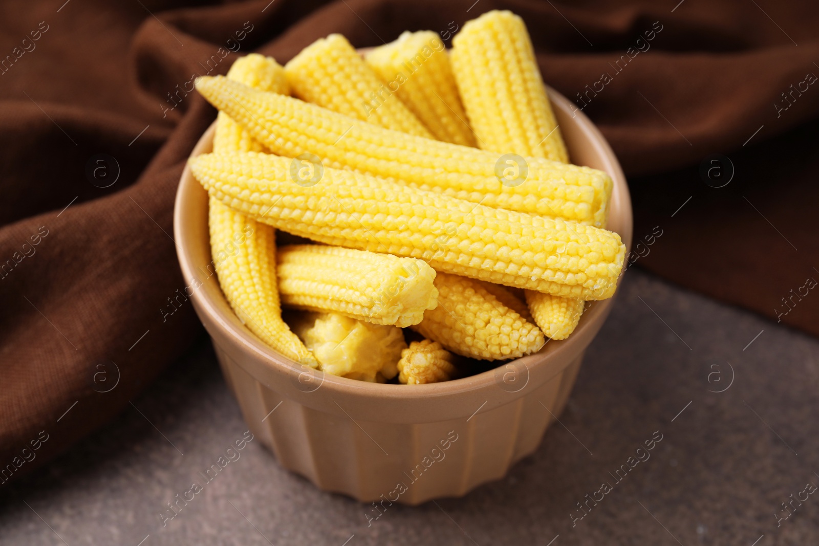 Photo of Tasty fresh yellow baby corns in bowl on brown table