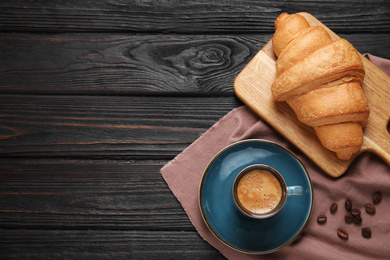 Photo of Tasty fresh croissant and coffee on black wooden table, flat lay. Space for text
