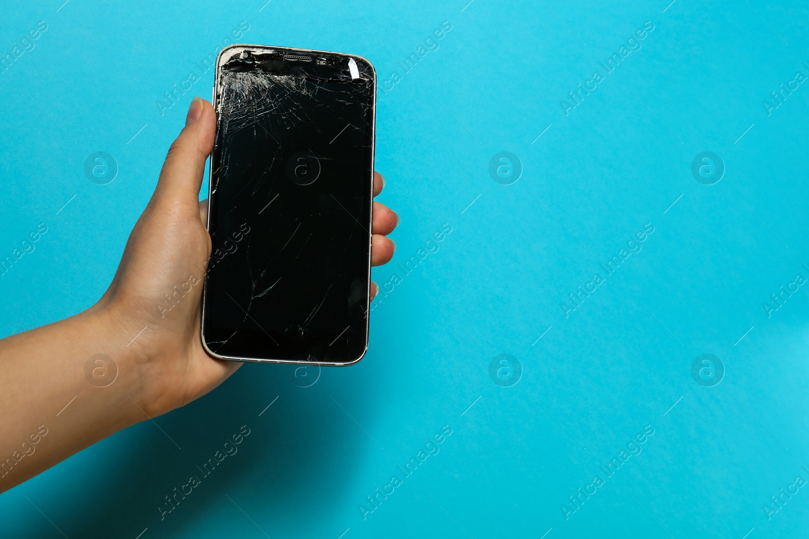 Photo of Woman holding damaged smartphone on light blue background, closeup with space for text. Device repairing