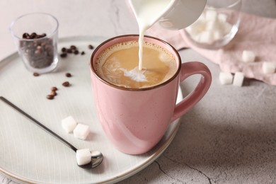 Photo of Pouring milk into cup with coffee on light grey textured table, closeup