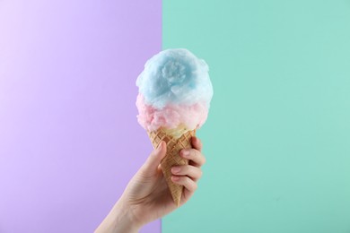 Photo of Woman holding waffle cone with cotton candy on color background, closeup