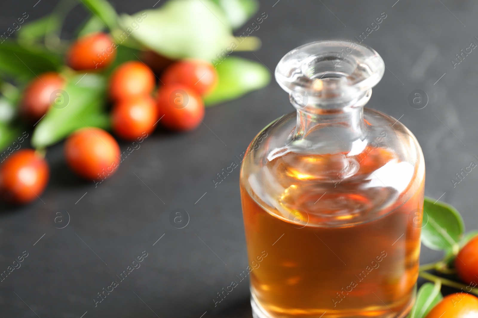 Photo of Glass bottle with jojoba oil and seeds on grey stone table, closeup. Space for text